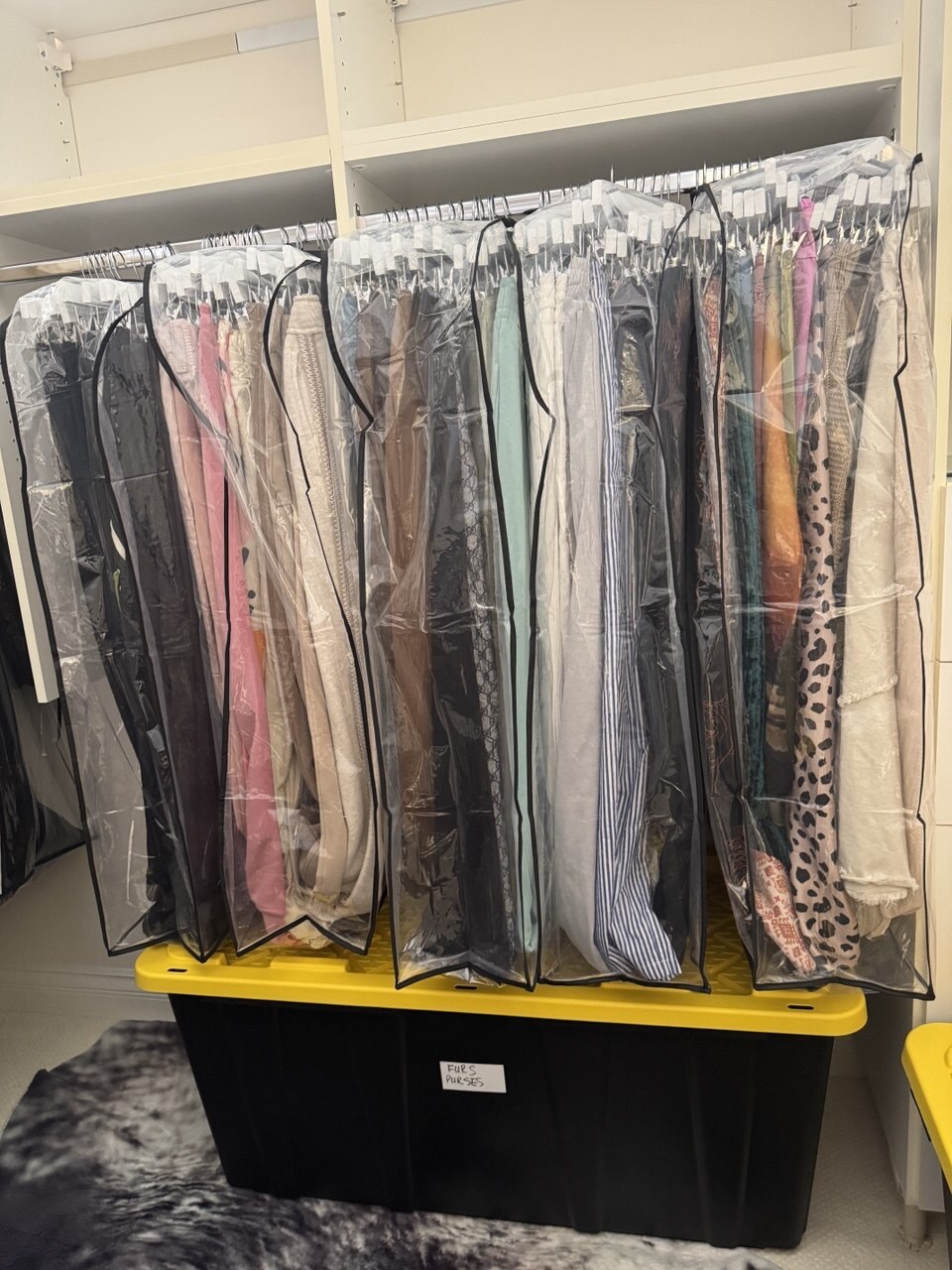 Dresses and coats packed into clear garment bags for a Las Vegas move, above a lidded bin hand-labelled for furs and purses