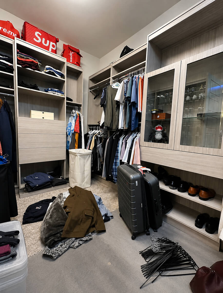 Disorganized walk-in wardrobe in a Las Vegas luxury home before Lifelystyle organizing — clothes on the floor, loose hangers, luggage blocking access to a custom built-in closet system