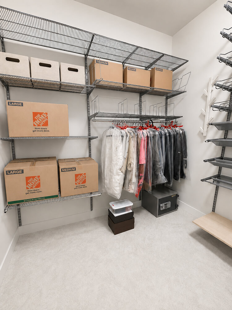 Move-in closet mid-process by Lifelystyle in Las Vegas — labeled moving boxes, dry-cleaned garments hung and protected, and a safe already placed — systematic Day One unpacking for luxury relocators